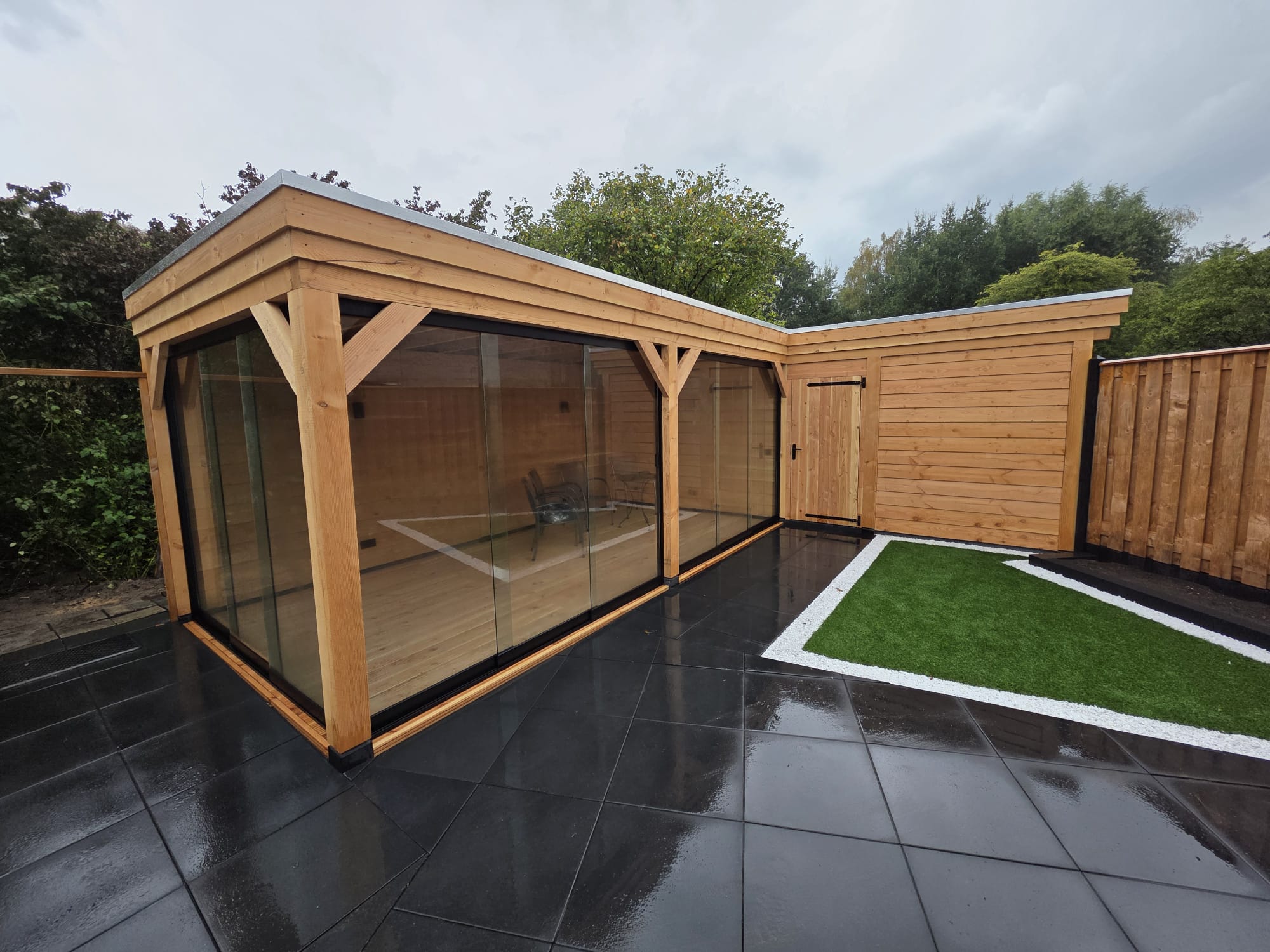 Houten overkapping met glasschuifwanden, vlonder en kunstgras in een tuin